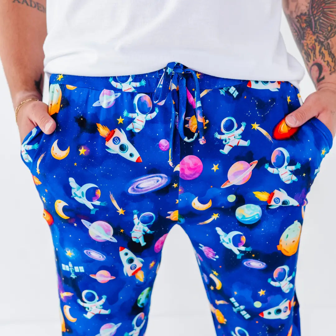 Close-up of royal blue drawstring pajama pants printed with astronauts, rockets, planets, and stars, worn with a white tee.